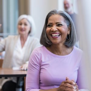 An attractive African American woman clasps her hands and smiles while her friend asks a question.